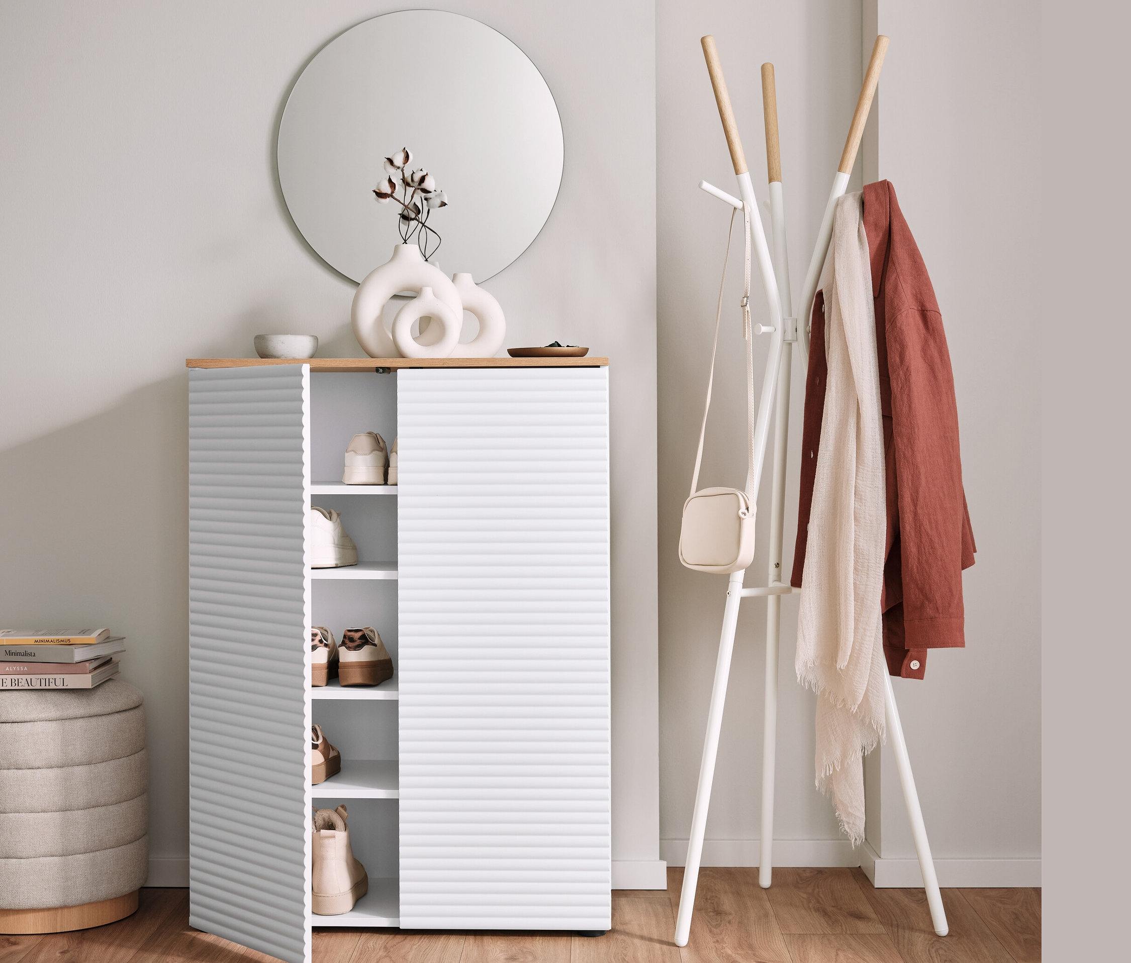 Schuhschrank mit offener Tür neben Garderobenständer und Pouf mit Stauraum.