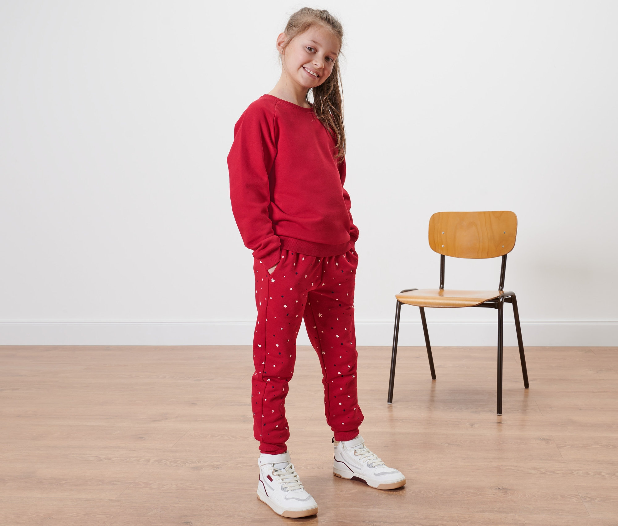 Mädchen trägt eine rote Kinder-Sweat-Kombi mit Sternen.