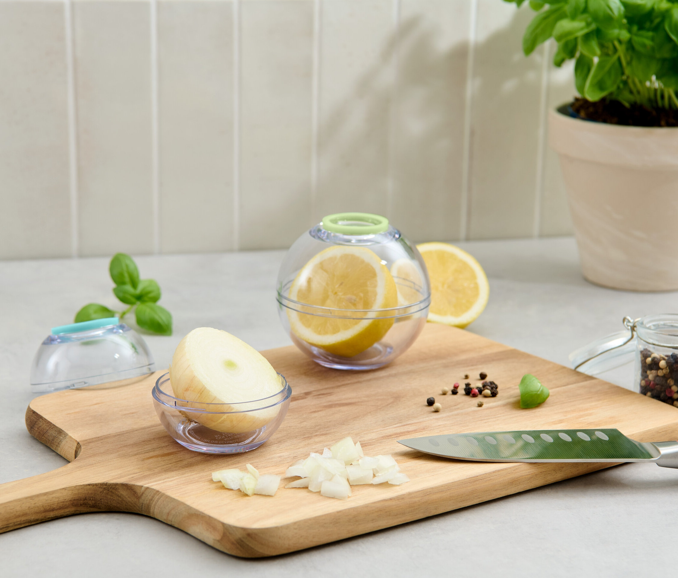 Zwei Frischhaltekugeln, eine mit Zitrone, die andere mit Zwiebel, liegen auf einem Schneidebrett.