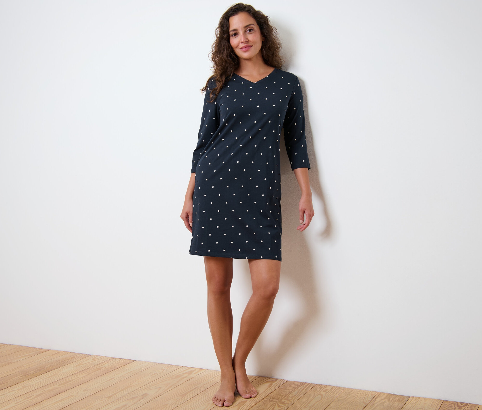 Frau steht und trägt ein Nachthemd mit Dreiviertelärmeln und Punkten.
