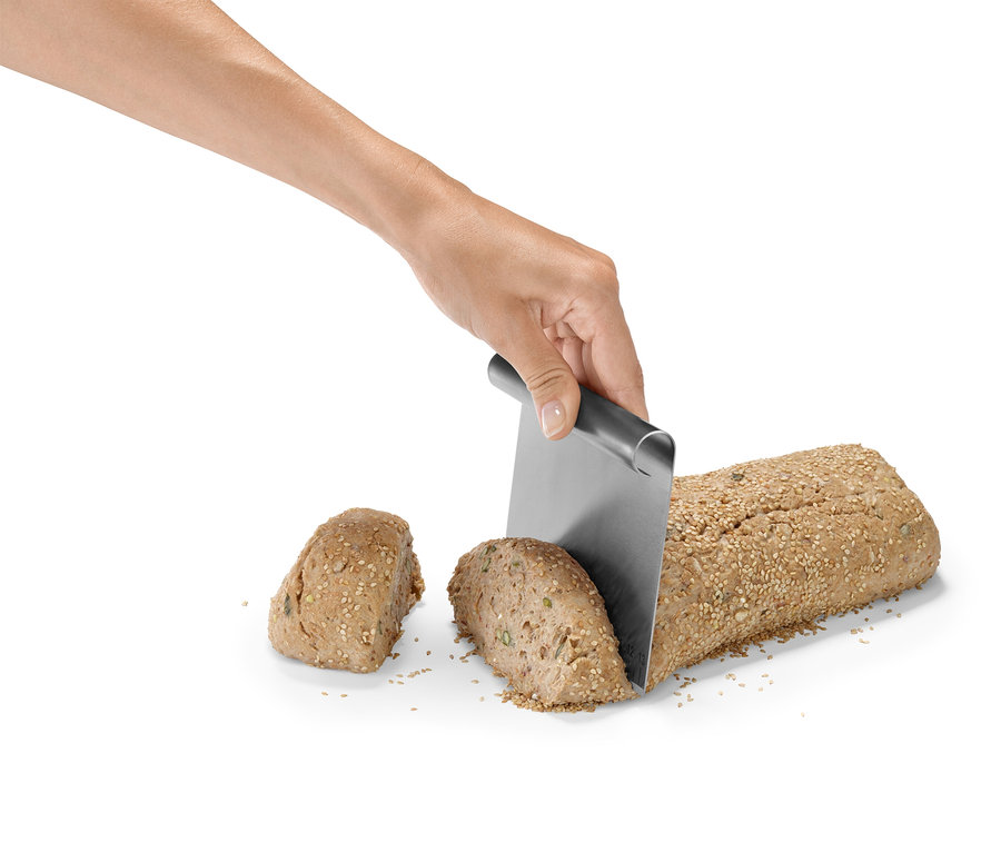 Eine Hand schneidet ein mit Samen bestreutes Brotlaib mit einem Metallmesser.