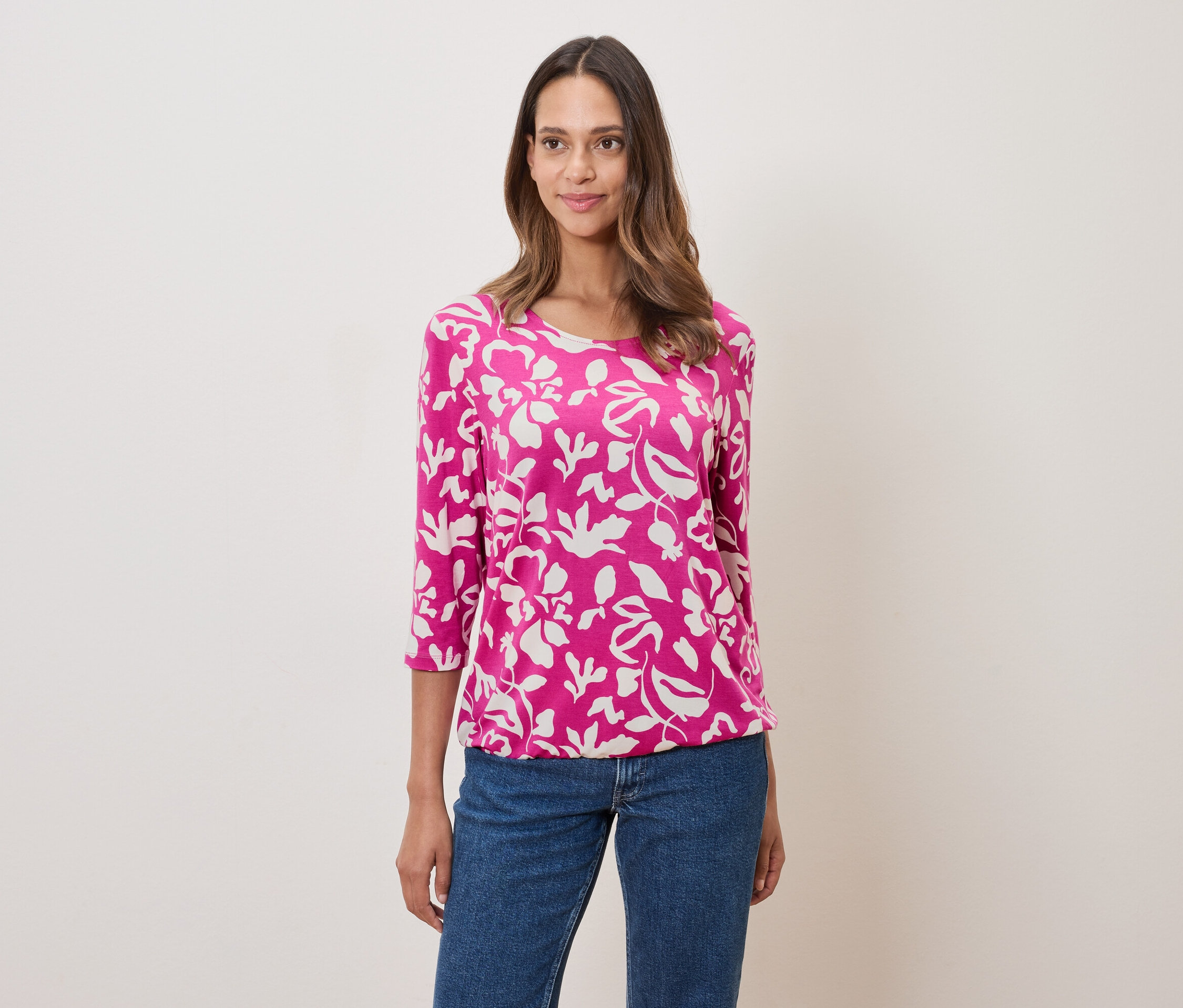Frau trägt ein pinkes, blumengemustertes Oberteil und Jeans.