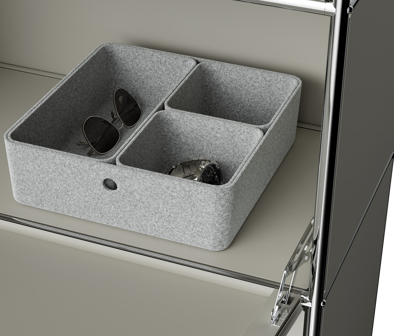 Eine graue Filzbox mit drei Fächern steht auf einem Regal. In einem Fach liegen eine Sonnenbrille und in einem anderen eine Armbanduhr.