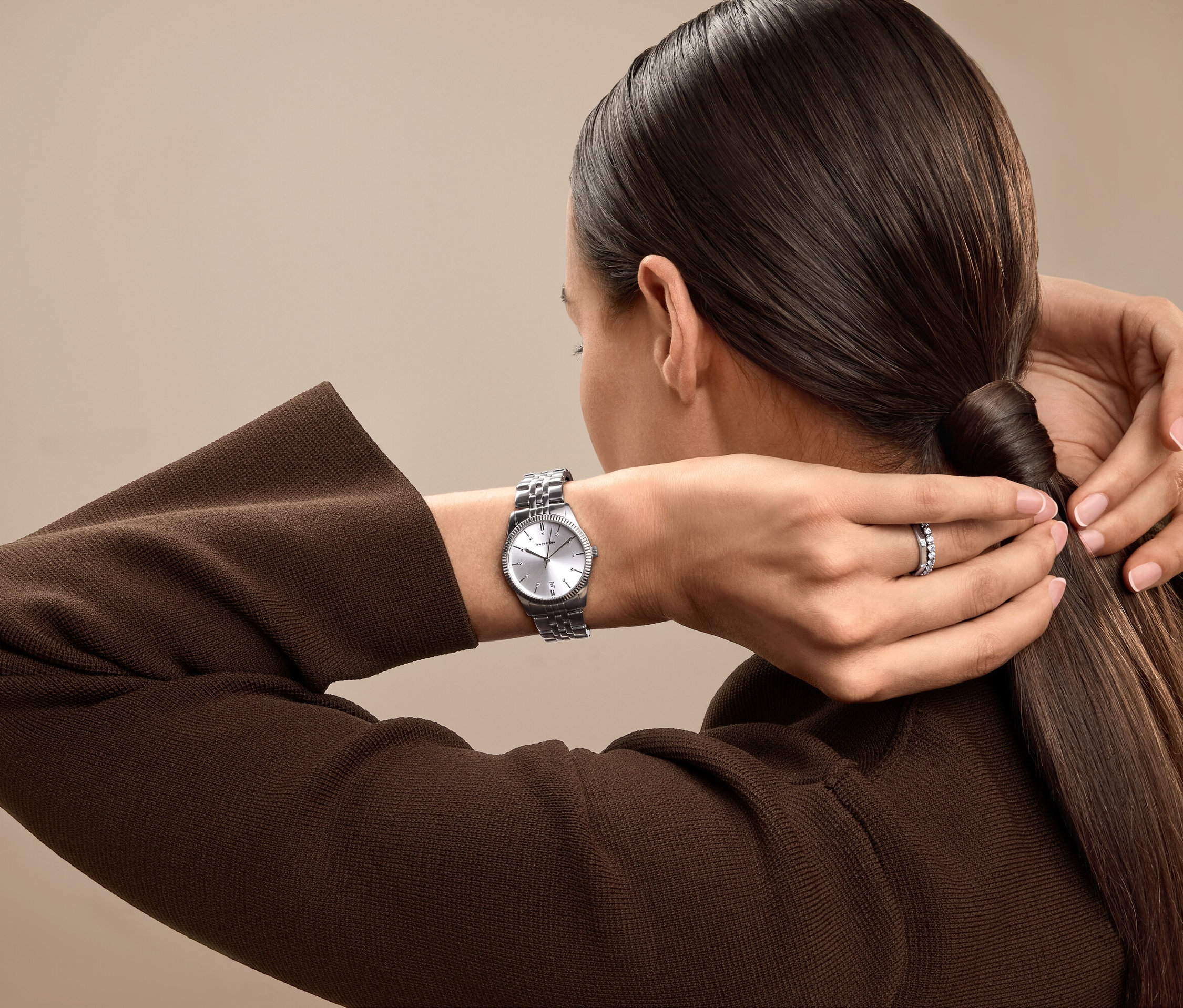 Frau bindet ihre Haare zu einem Pferdeschwanz zusammen, trägt eine silberne Uhr und einen Ring.
