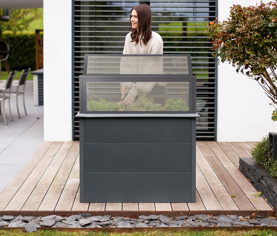 Frau erntet Salat in einem anthrazitfarbenen Hochbeet Schneckenschutz mit Frühbeetaufsatz und einem Metall-Hochbeet mit Stauraum und Aufsatz.
