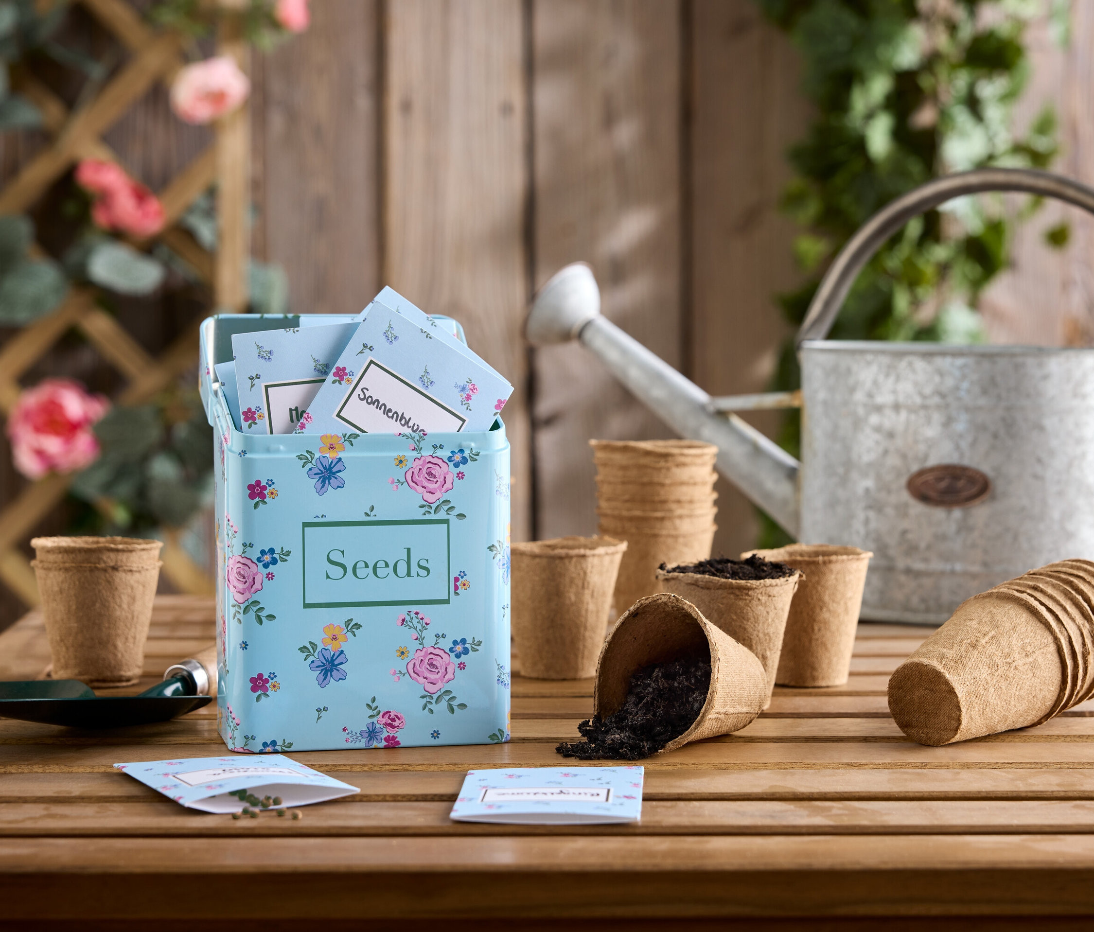 Blumensamen-Set auf Holztisch mit Zinngießkanne und Anzuchttöpfen.
