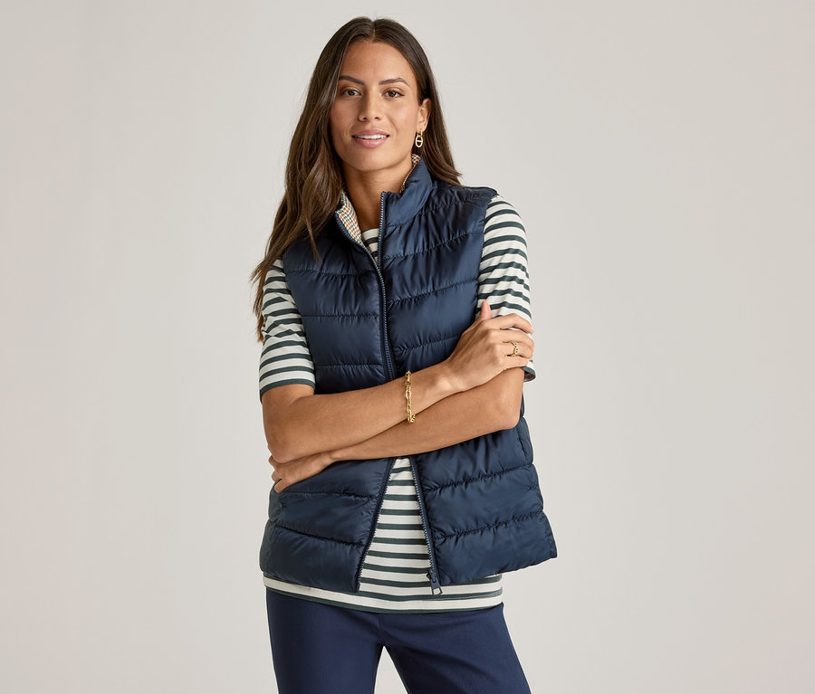 Frau mit verschränkten Armen trägt marineblaue Weste über grün gestreiftem Halbarmshirt.