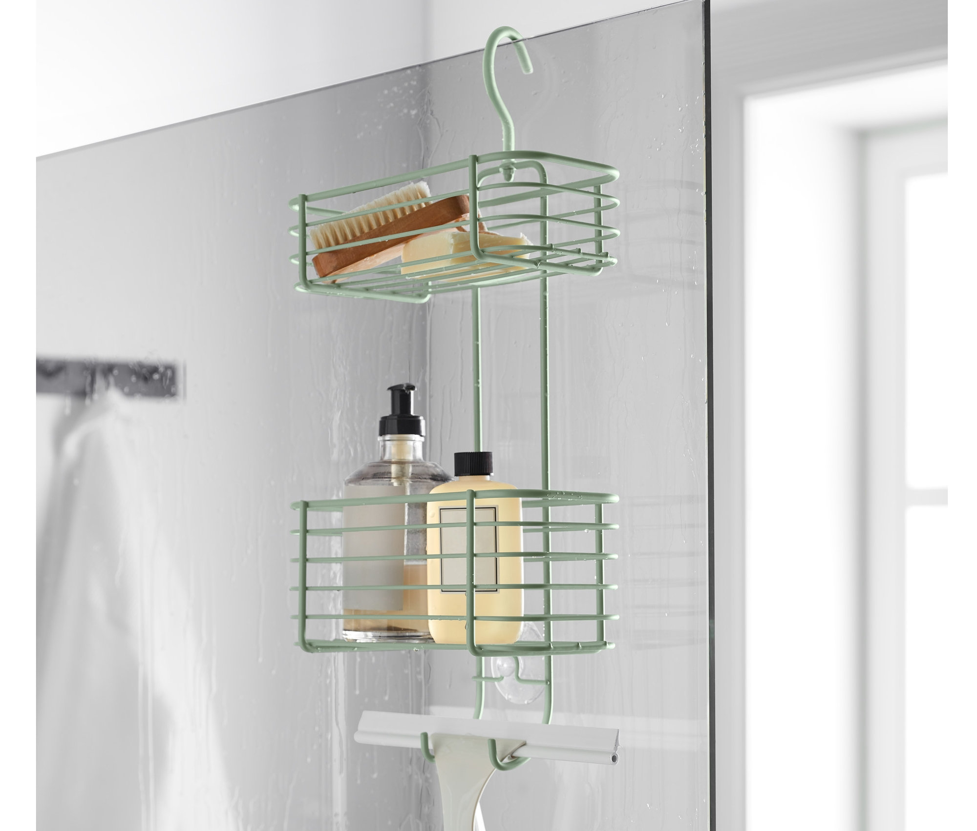 Ein grünes, hängendes Duschregal hängt an einer Duschwand. Im Regal befinden sich eine Bürste, eine Flasche und ein Abzieher.