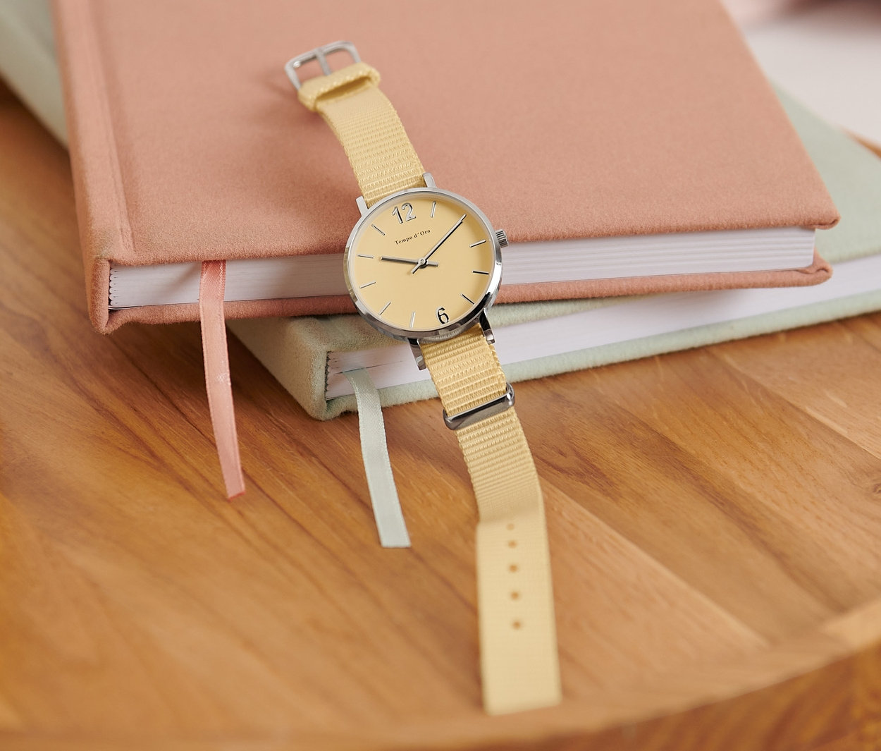 Eine gelbe Quarz-Armbanduhr aus 316L-Edelstahl liegt auf zwei Notizbüchern neben einer brennenden Kerze.