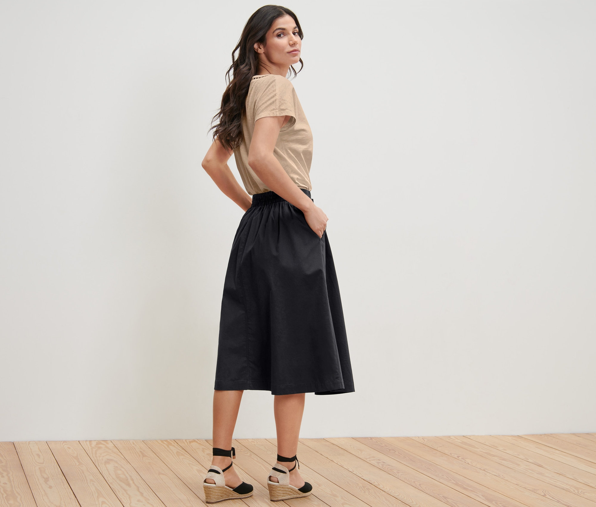 Frau posiert in beigem T-Shirt und schwarzem Popeline-Rock.