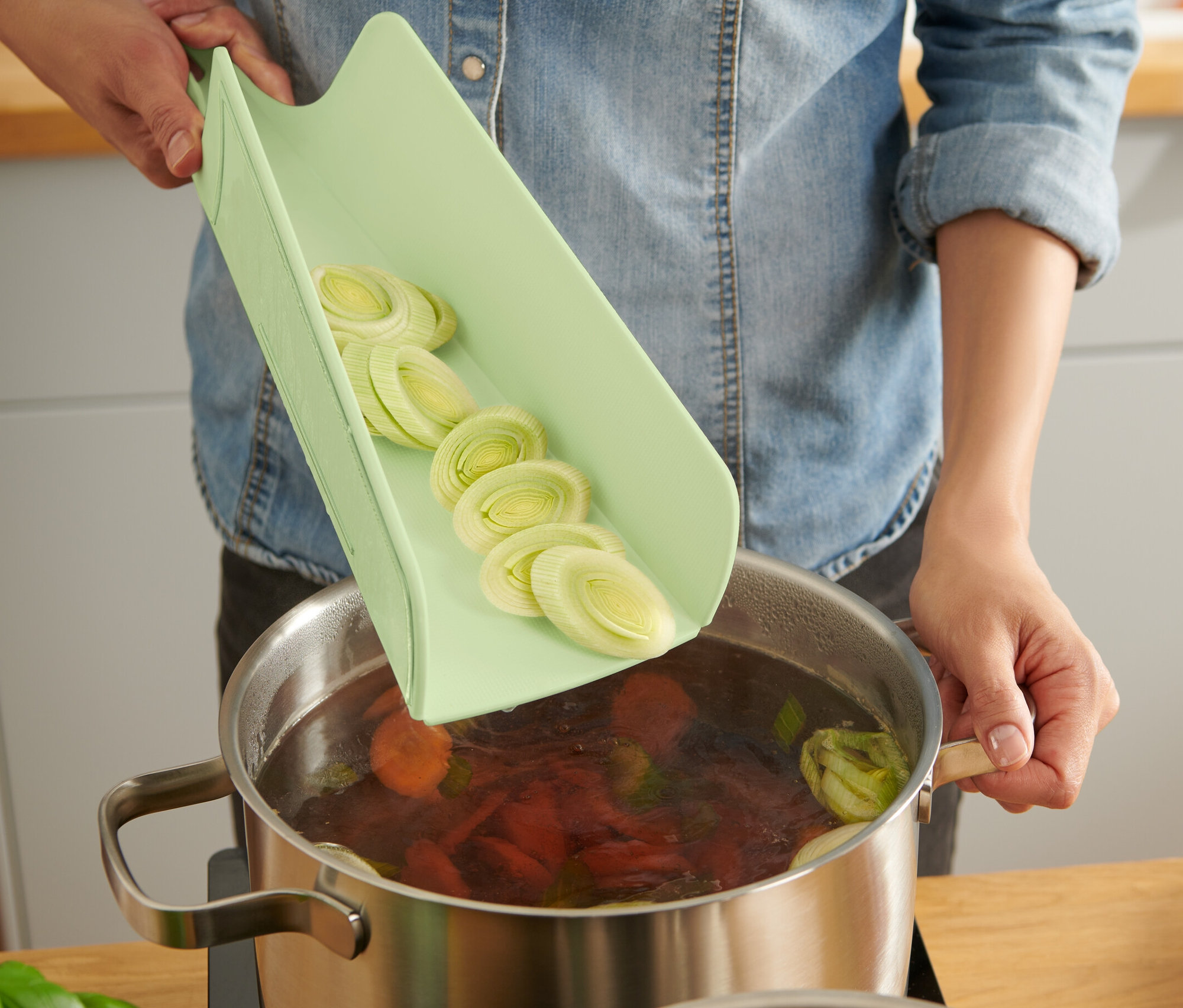 Frau gibt geschnittenen Lauch von einem faltbaren Schneidebrett in einen Topf mit Suppe.