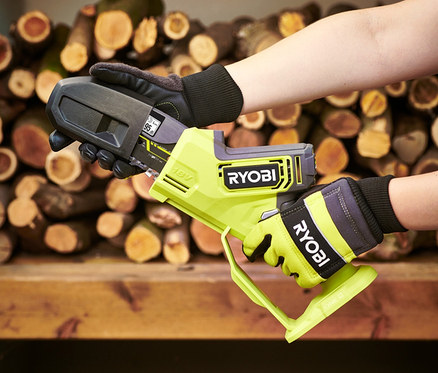 Person hält eine RYOBI 18 V One+ Brushless Akku-Einhand-Kettensäge (ohne Akku und Ladegerät) mit Handschuhen vor einem Holzstapel.