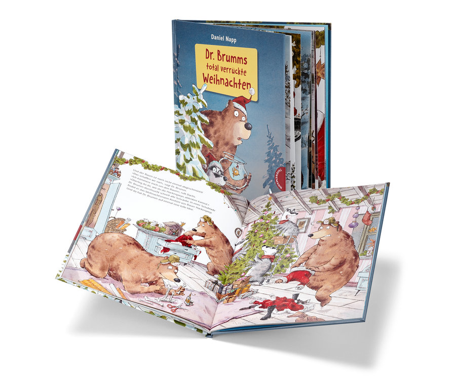 Offenes Buch "Dr. Brumms total verrückte Weihnachten" mit Illustrationen von Bären und Waschbären, die einen Weihnachtsbaum schmücken, im Hintergrund eine weitere Ausgabe des Buchs.
