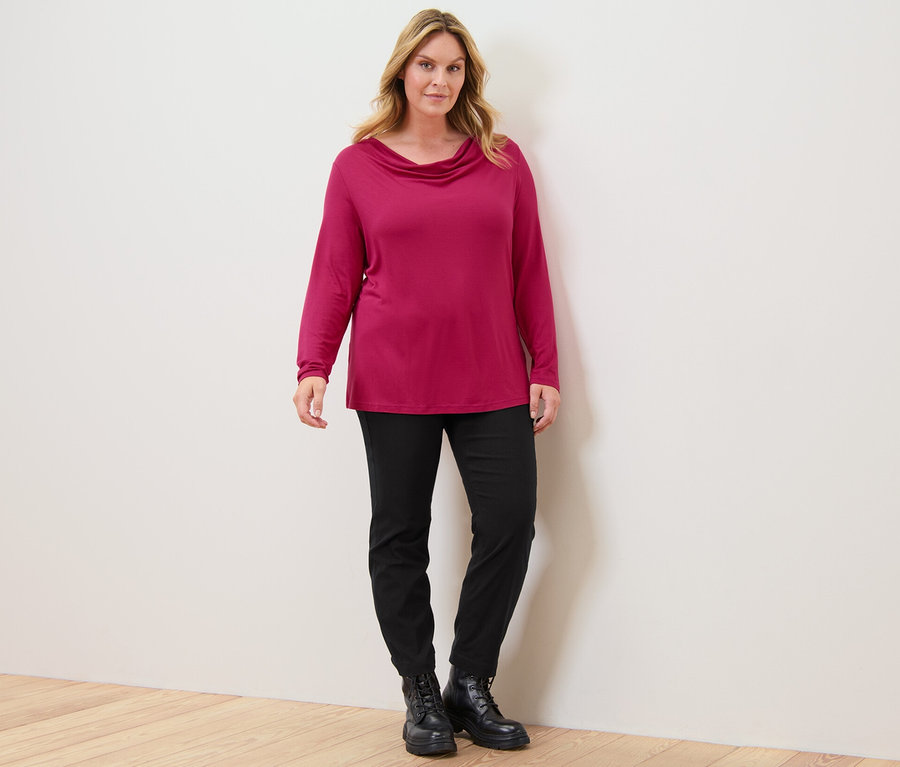 Frau steht und trägt ein Blusenshirt mit Wasserfallausschnitt und eine Bengalin-Hose.