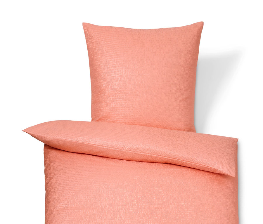 Korallenfarbene Seersucker-Bettwäsche in Normalgröße und Übergröße liegt auf einem weißen Hintergrund.