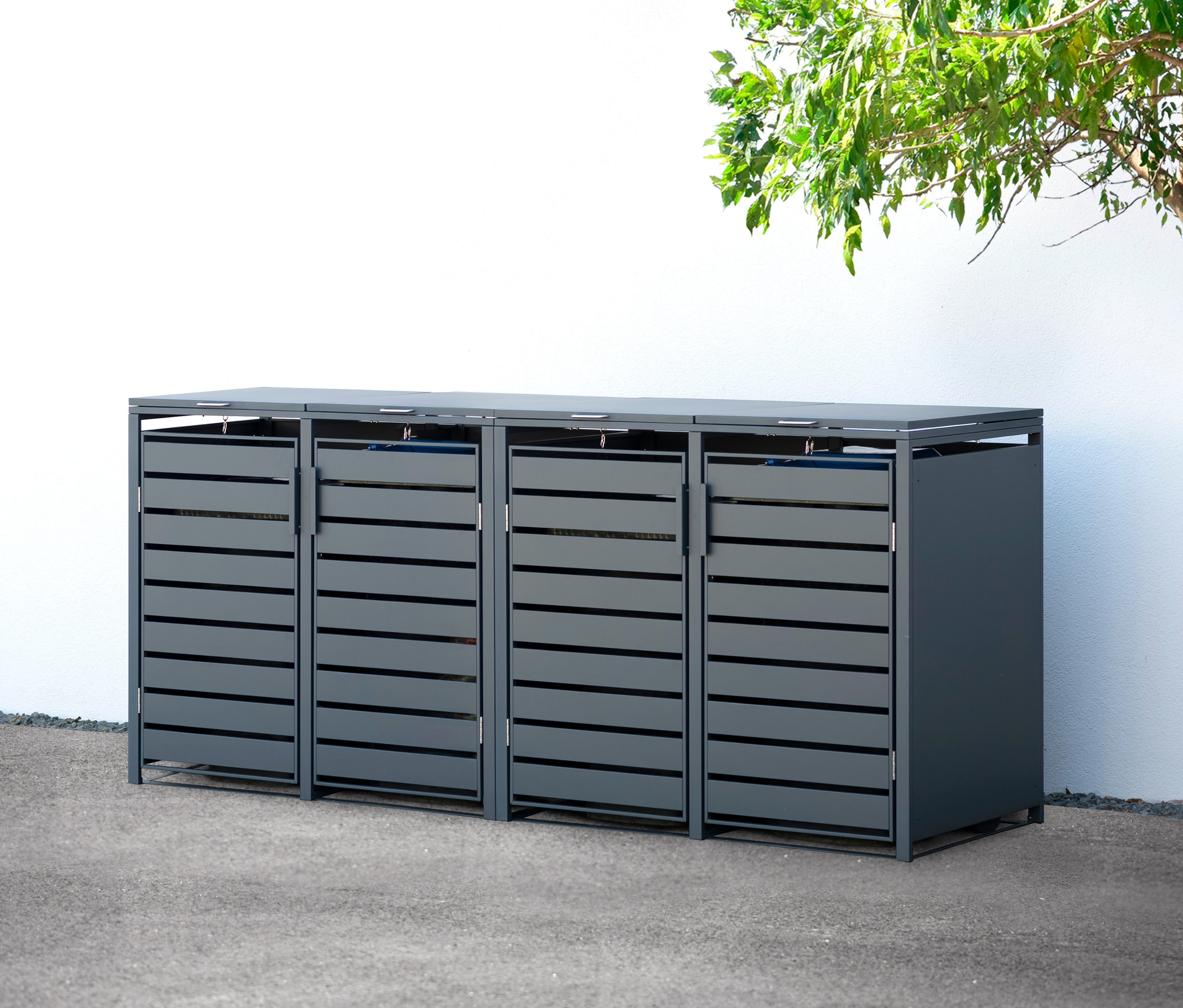 Eine Mülltonnenbox aus Stahl mit 4 Fächern steht draußen neben einem Baum.