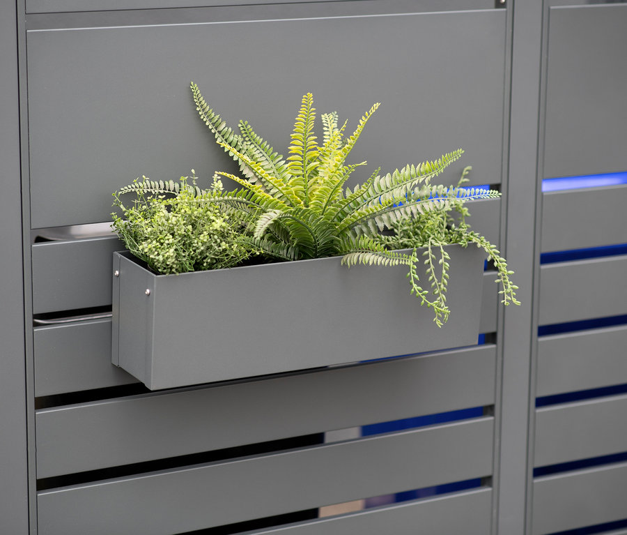 Grauer Blumenkasten aus Stahl mit Pflanzen an einem grauen Zaun.