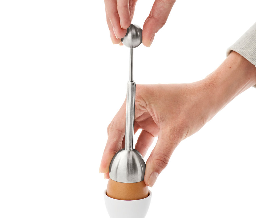 Hände verwenden einen Eierköpfer auf einem Ei in einem weißen Eierbecher.