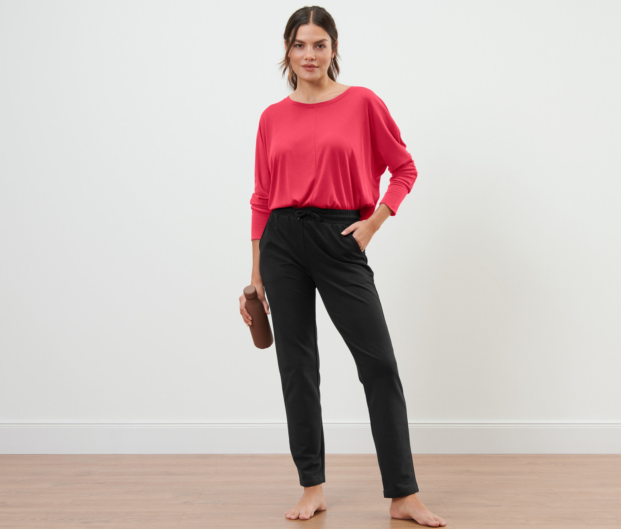 Frau steht und hält eine Wasserflasche, trägt eine schwarze Sweathose.