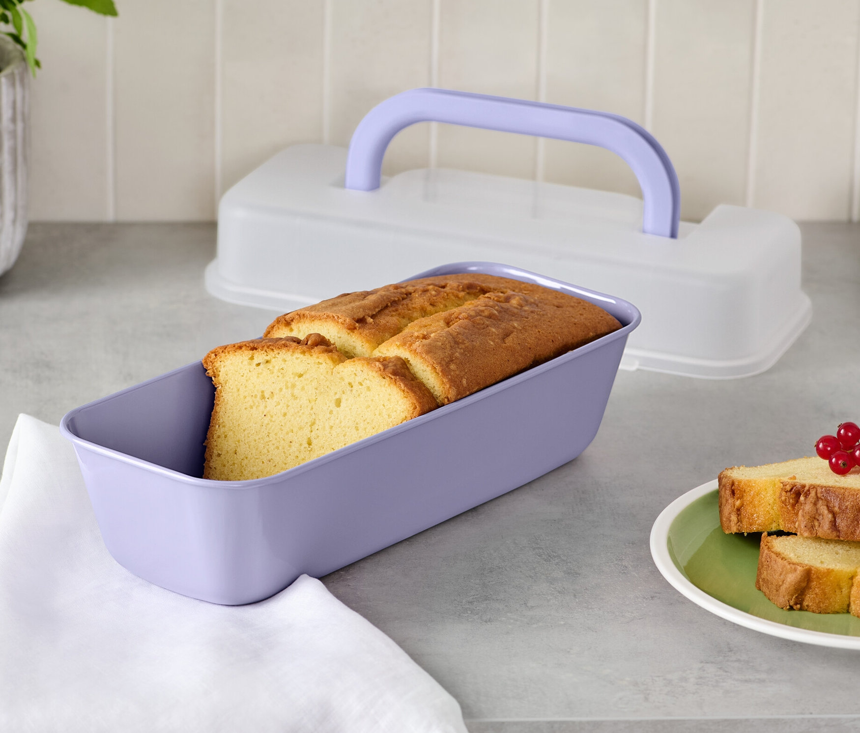 Brot in lila Kastenform mit Deckel und zwei Brotscheiben auf einem Teller.