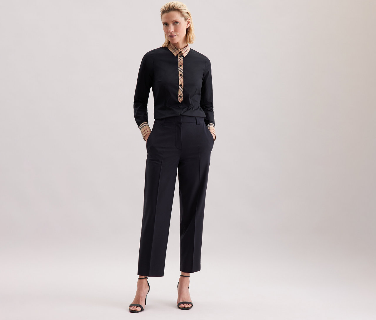 Frau in schwarzer Seidensticker Popeline-Bluse mit Karodetail und dunkler Hose posiert.