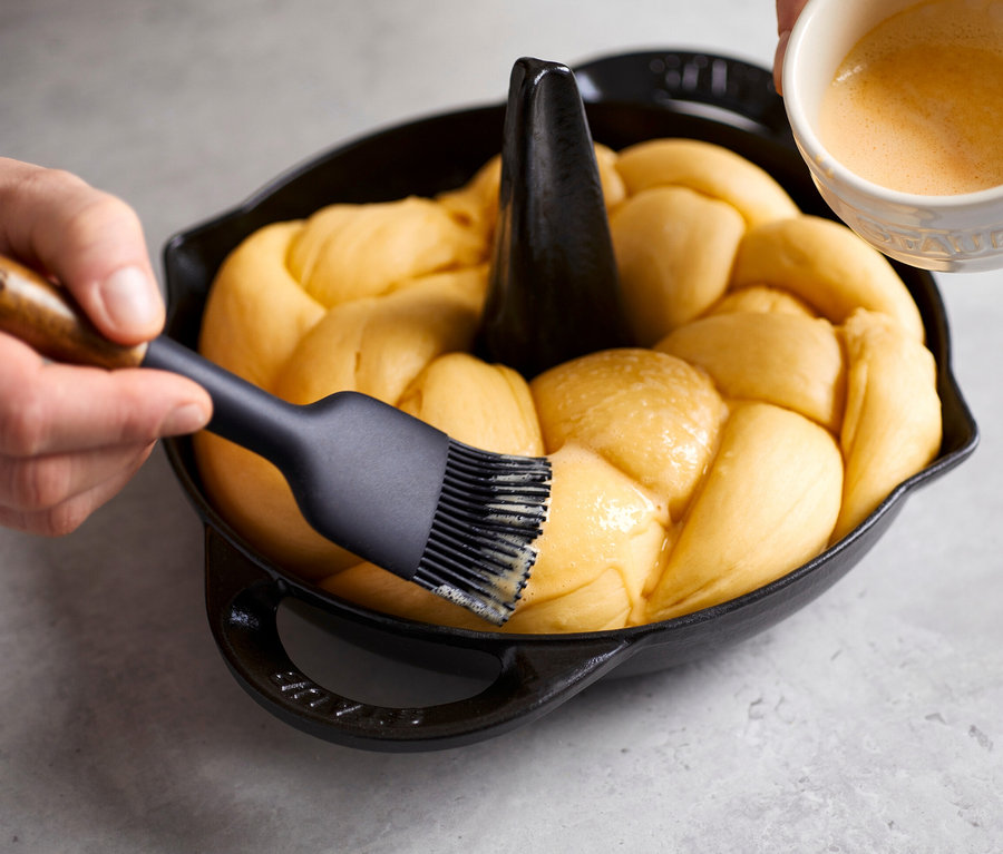 Ein Zopf wird in einem schwarzen STAUB Hähnchen-Bräter gebacken und mit Ei bestrichen.