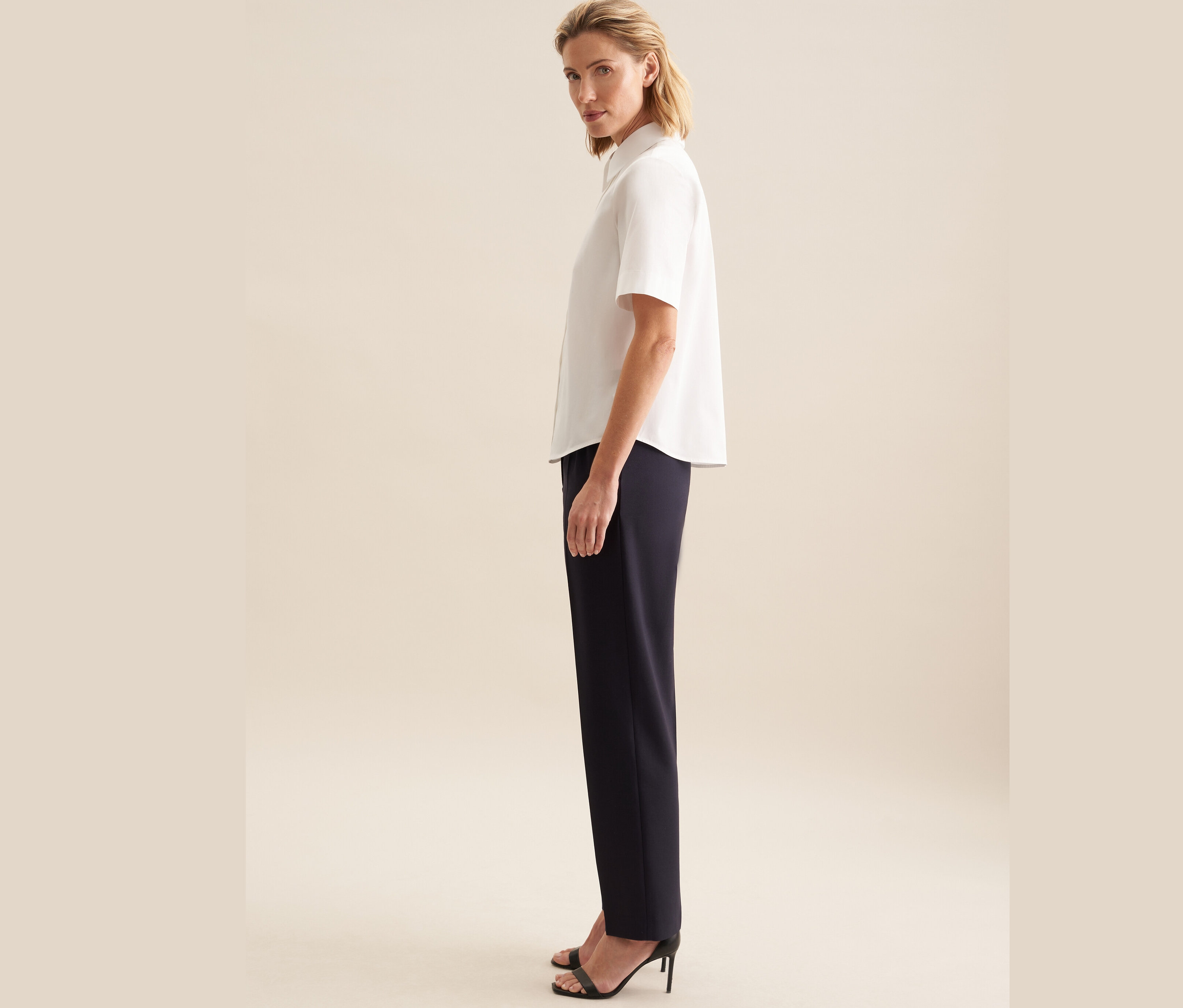 Frau posiert in weißer Seidensticker Kurzarm-Bluse und dunkelblauer Hose.