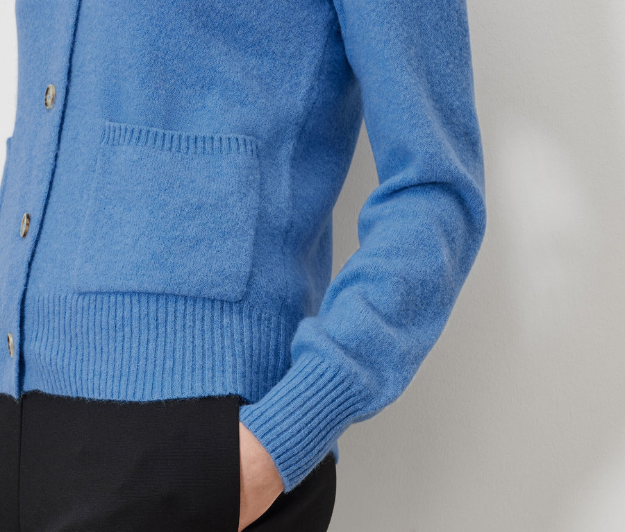 Detailansicht einer blauen Strickjacke mit Tasche und schwarzer Hose.