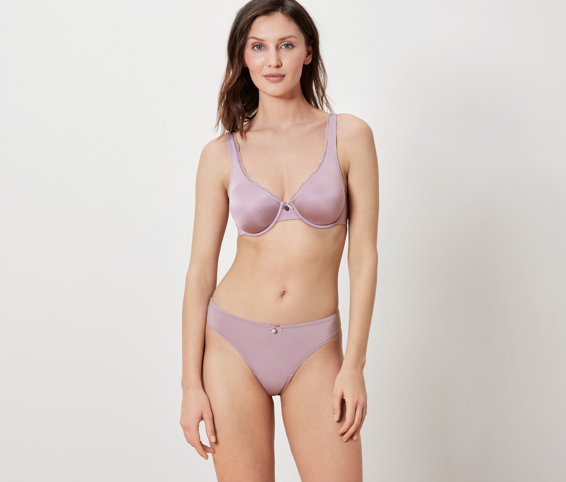 Frau posiert vor einem weißen Hintergrund in einem passenden lila BH und Höschen.