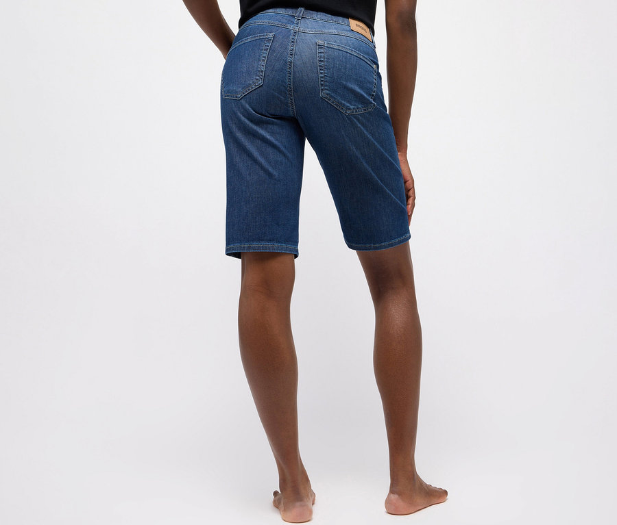 Eine Person von hinten, die mittlere blaue Angels Jeans »Bermuda Turn-Up« im Straight Fit trägt und barfuß steht.