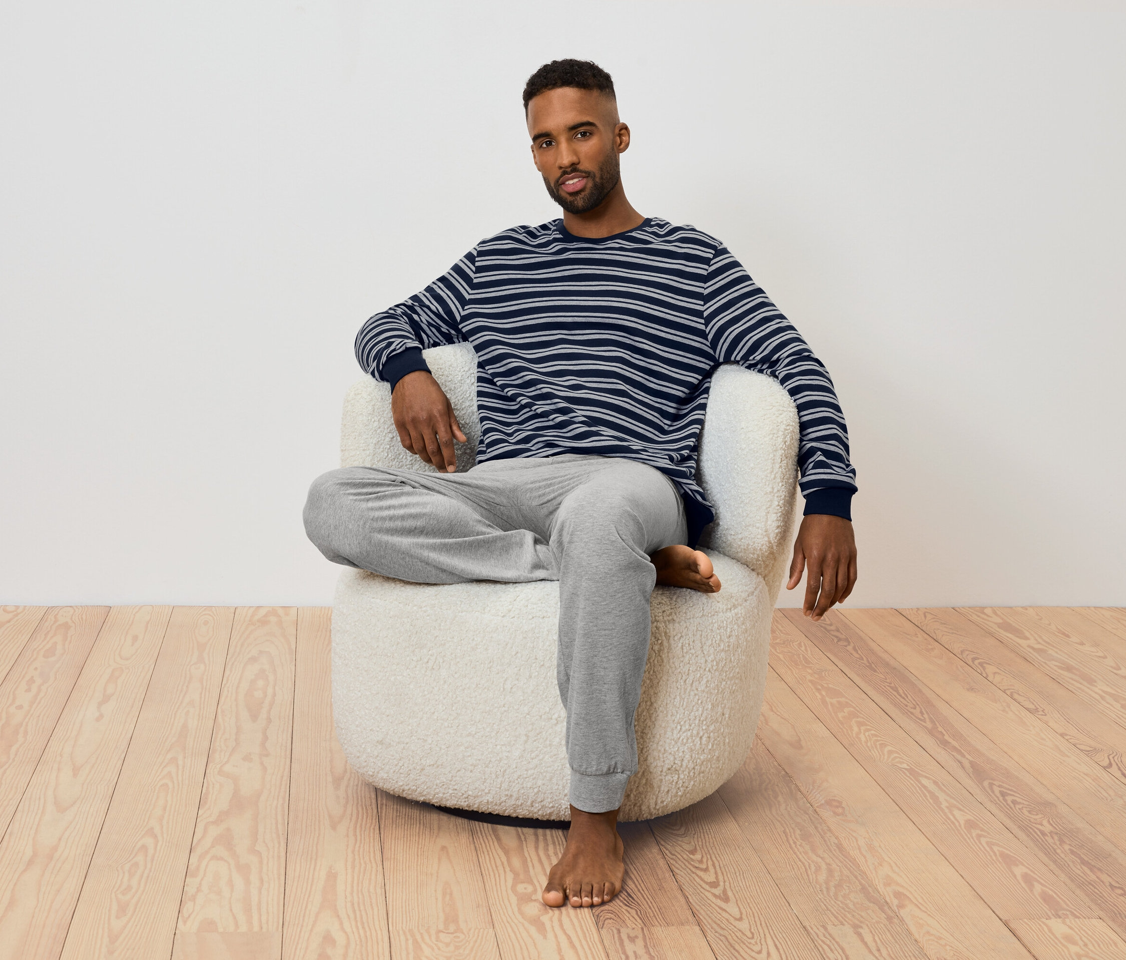 Mann sitzt in einem Sessel. Er trägt ein gestreiftes Langarmshirt und eine graue Jogginghose.