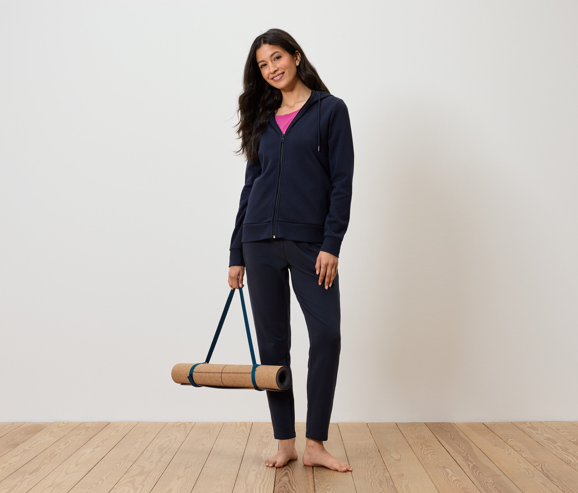 Frau hält Yogamatte, trägt marineblauen Trainingsanzug und rosa Tanktop.