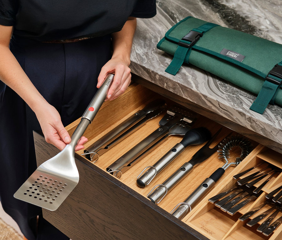 Frau öffnet eine Schublade mit Grillbesteck und einem grünen Grillbesteck-Etui.