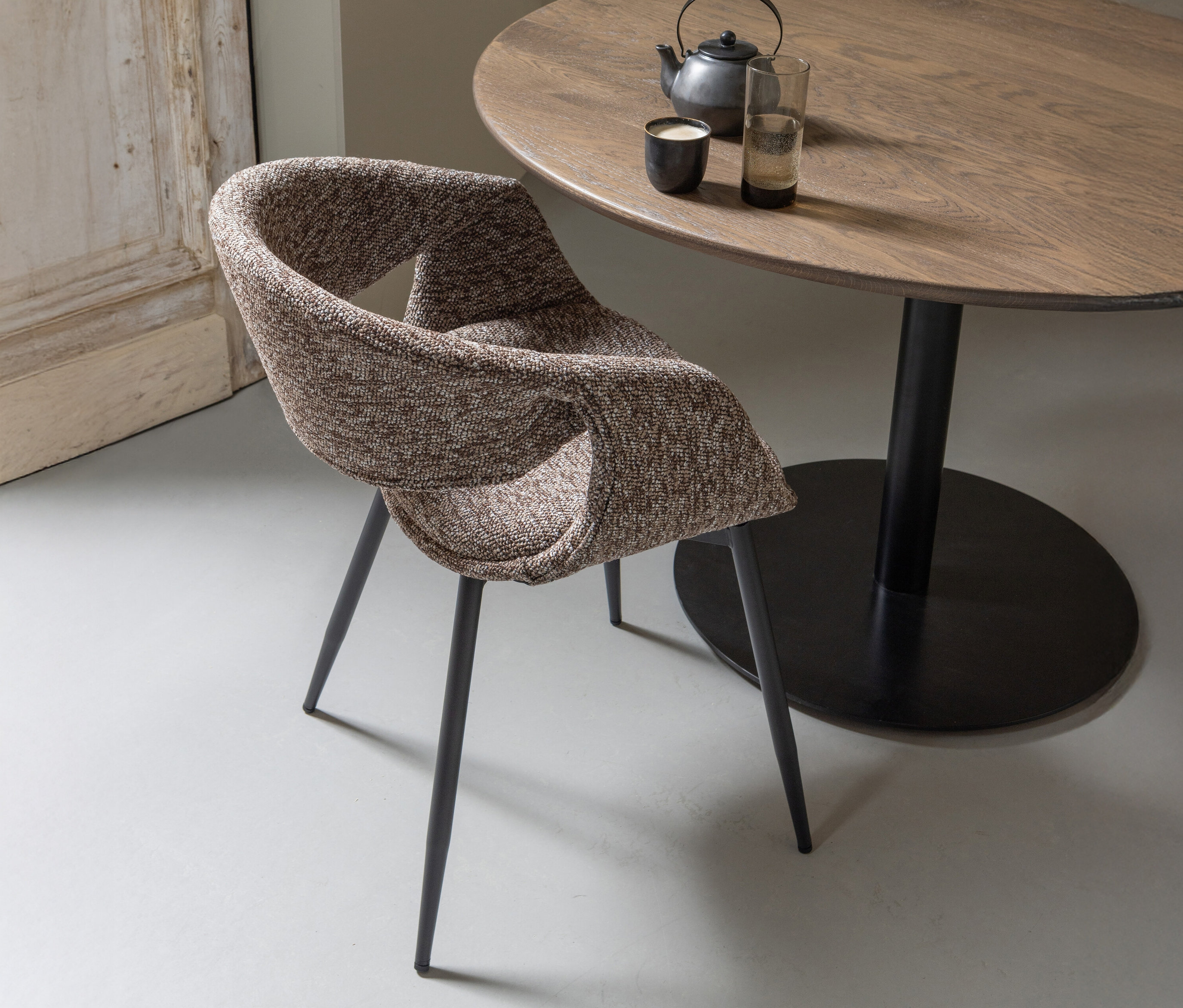 Ein brauner WOOOD Esszimmerstuhl »Yossi« mit Metallfuß aus einem 2er-Set steht an einem Holztisch mit Geschirr.