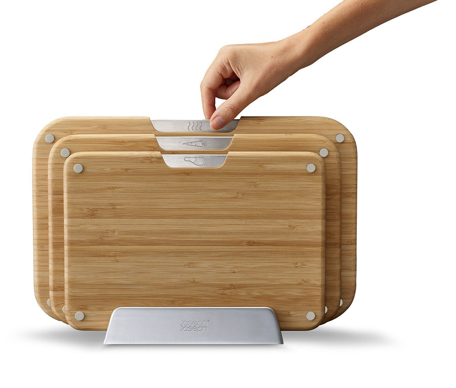 Eine Hand greift nach einem der Bambus-Schneidebretter, die in einem Halter stehen.