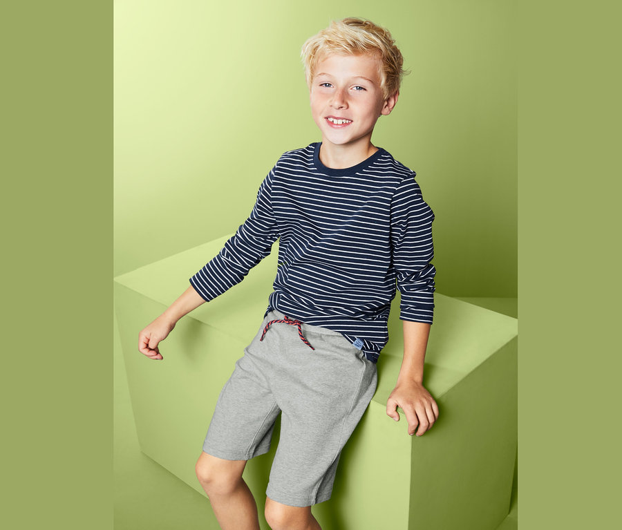 Ein Junge sitzt auf einem grünen Würfel und trägt ein gestreiftes T-Shirt und Sweatshorts.