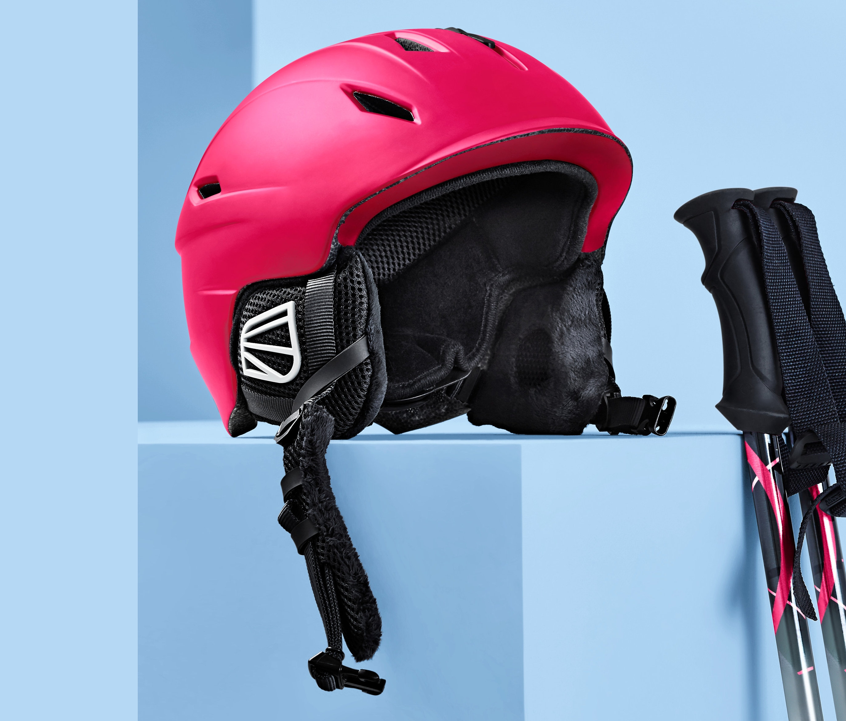 Ein roter In-Mould-Ski- und Snowboardhelm und Skistöcke auf blauem Grund.