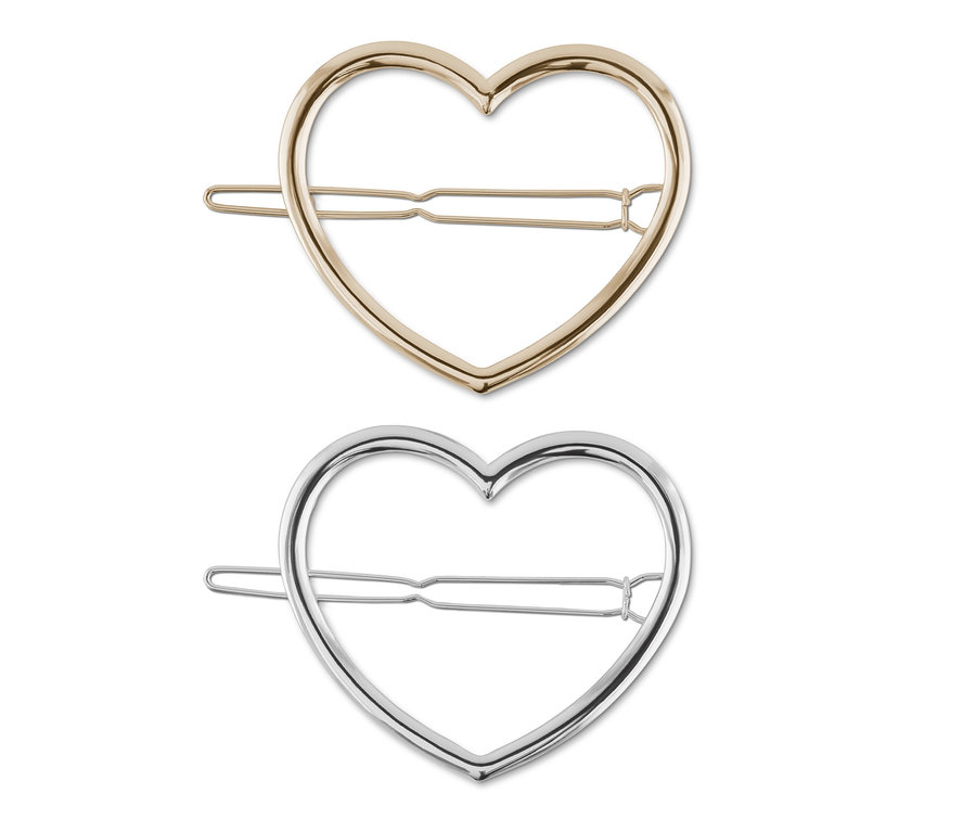 Zwei Haarspangen im Herzdesign, eine goldene und eine silberne, liegen auf einem weißen Hintergrund.