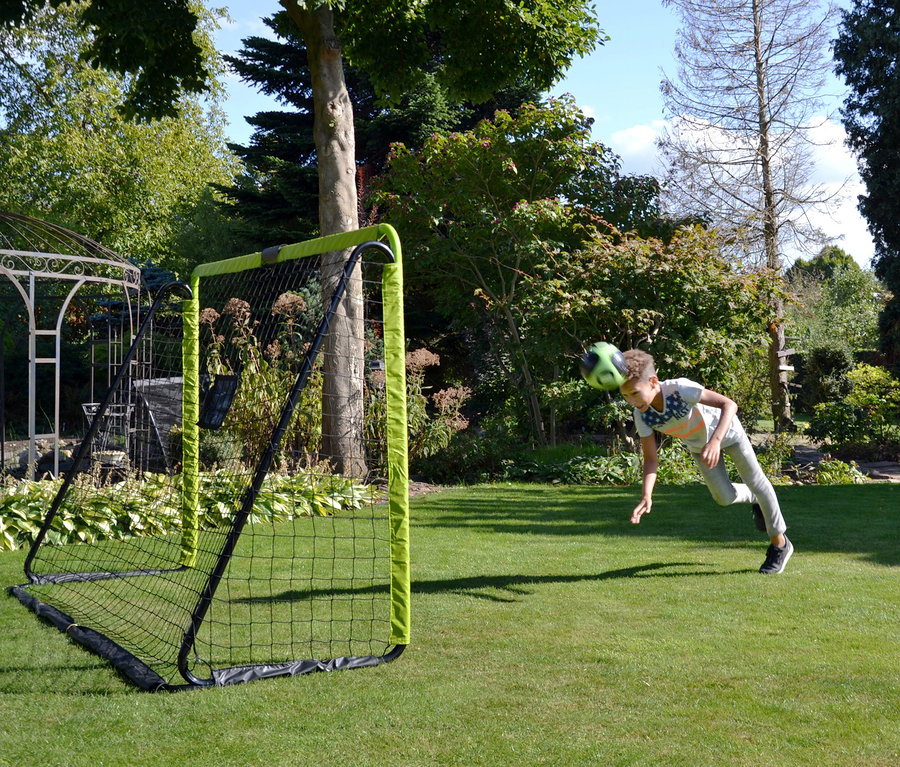 Junge köpft einen grünen Fußball in das EXIT Fußballtor »Tempo 1800« auf dem Rasen.