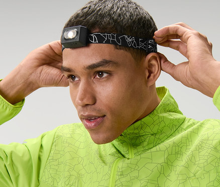 Mann justiert eine Stirnlampe auf seiner Stirn und trägt eine grüne Jacke.