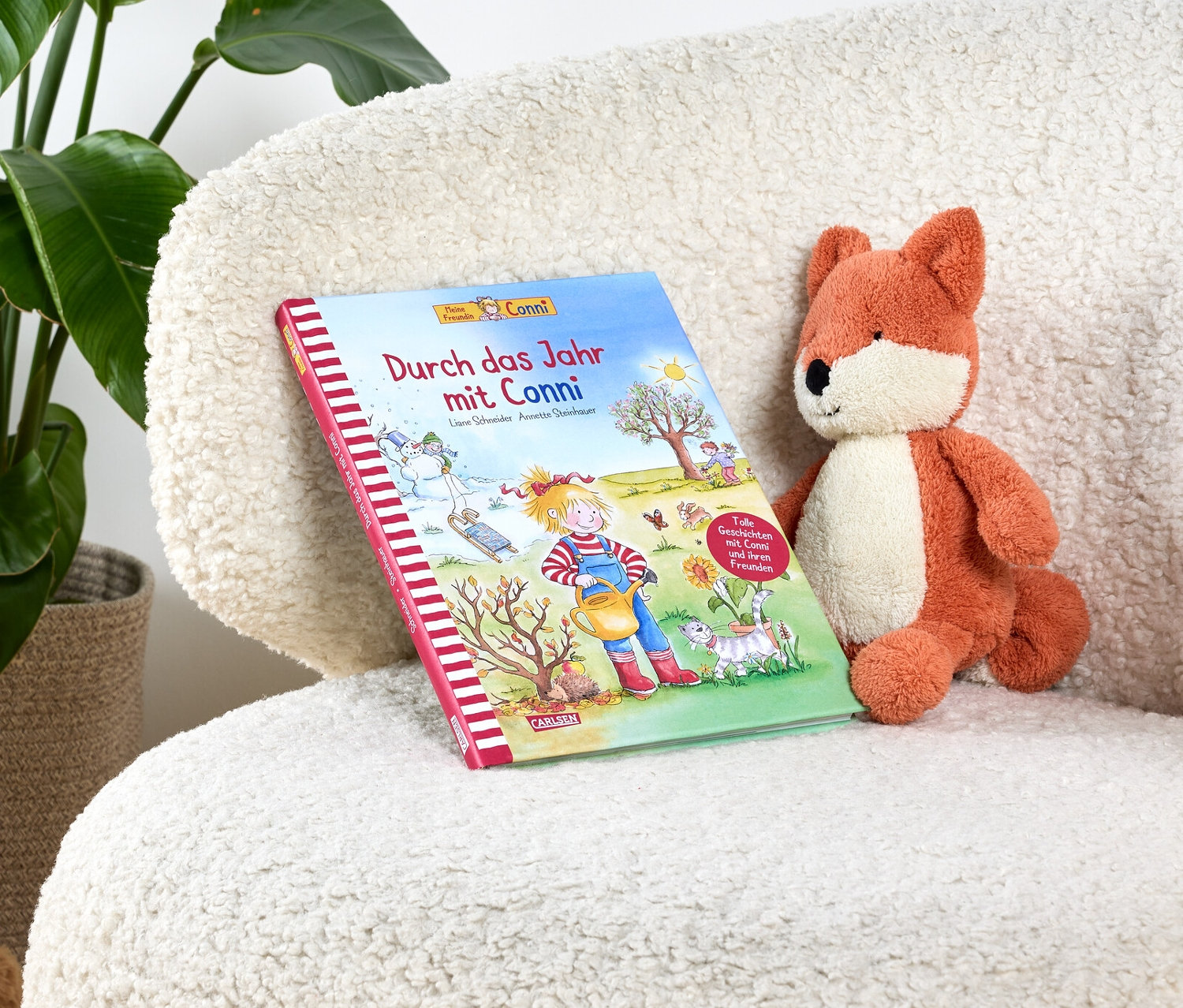 Das Buch »Durch das Jahr mit Conni« liegt auf einem weißen, zotteligen Sessel neben einem Stofffuchs.