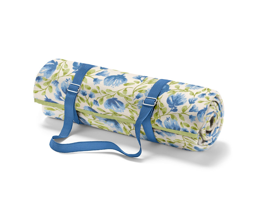 Eine zusammengerollte kleine Picknickdecke mit blauen Blumen und grünen Stängeln, die mit blauen Riemen befestigt ist.