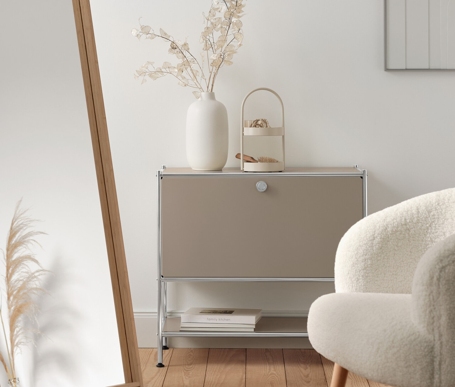 Interieur mit beige farbenem Sideboard Metall »CN3« mit Klappe, Standspiegel mit Rahmen aus Bambus und Bouclé-Sessel mit Holzbeinen.