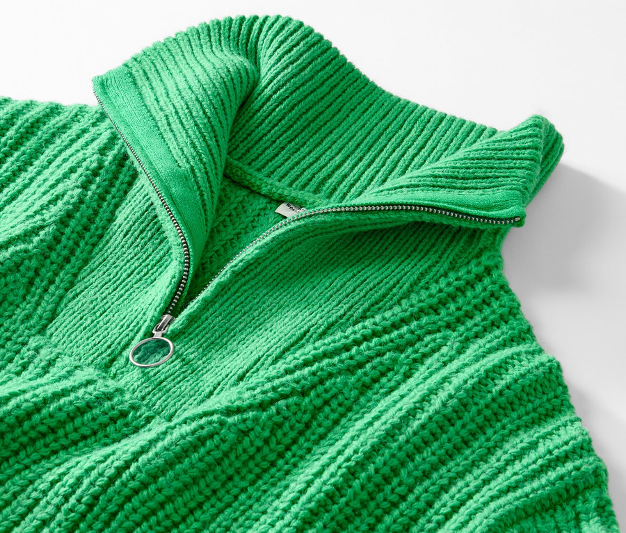 Detailansicht eines grünen Grobstrick-Troyers mit geöffnetem Reißverschluss.