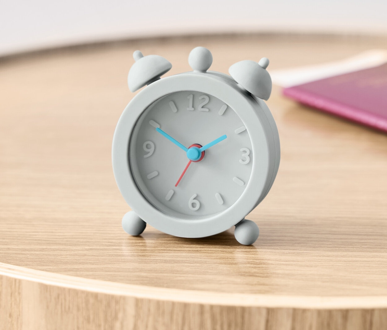 Ein grauer Reisewecker steht auf einem Holztisch neben einem Reisepass.