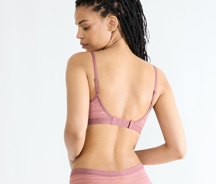 Frau mit Afro-Zöpfen, mit dem Rücken zur Kamera, trägt einen rosa Spitzen-BH und Höschen.