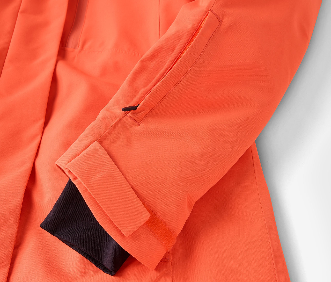 Detail einer orangefarbenen Jacke mit schwarzem Bündchen und Reißverschlusstasche.