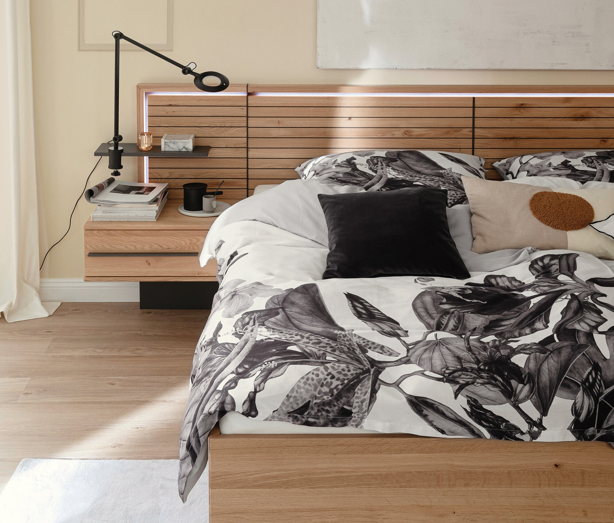 Bett mit hölzernem Kopfteil mit integrierter Beleuchtung und floraler Bettwäsche.