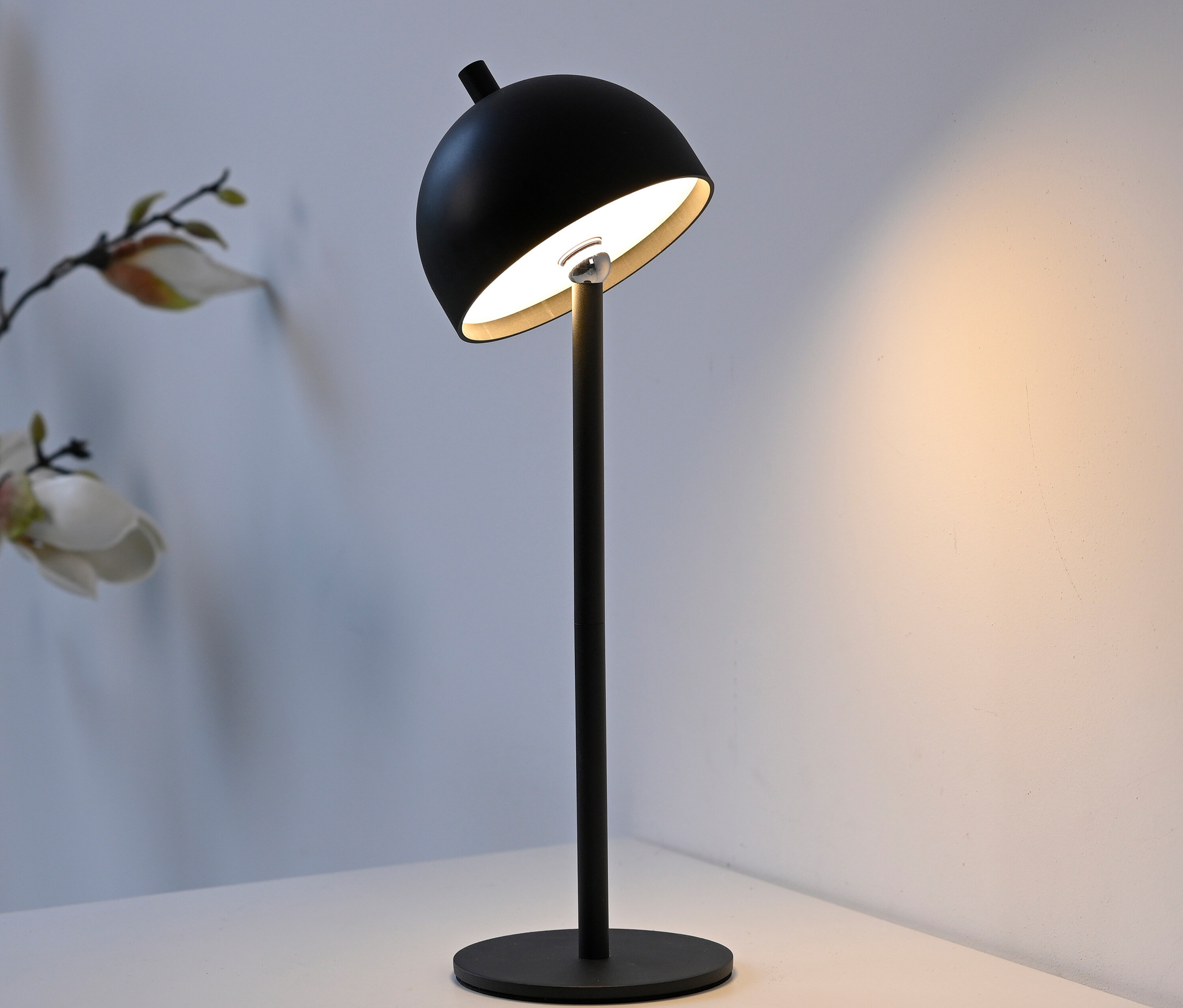Eine schwarze Tischleuchte mit rundem Lampenschirm und Metallfuß steht auf einem weißen Tisch.