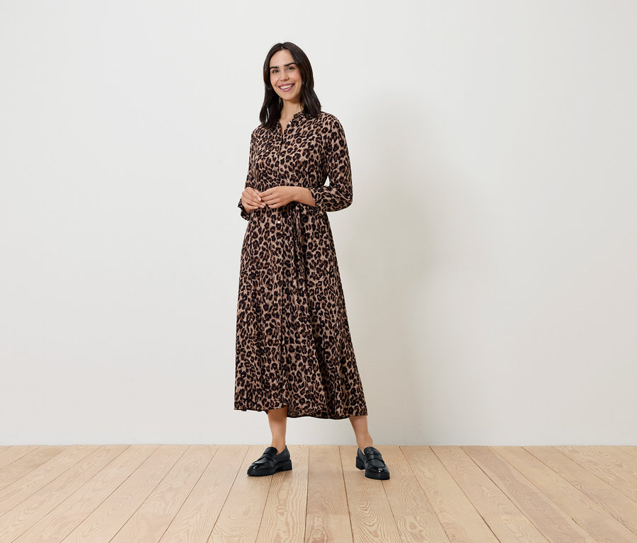 Eine Frau posiert in einem gemusterten, langärmligen Kleid und schwarzen Schuhen.